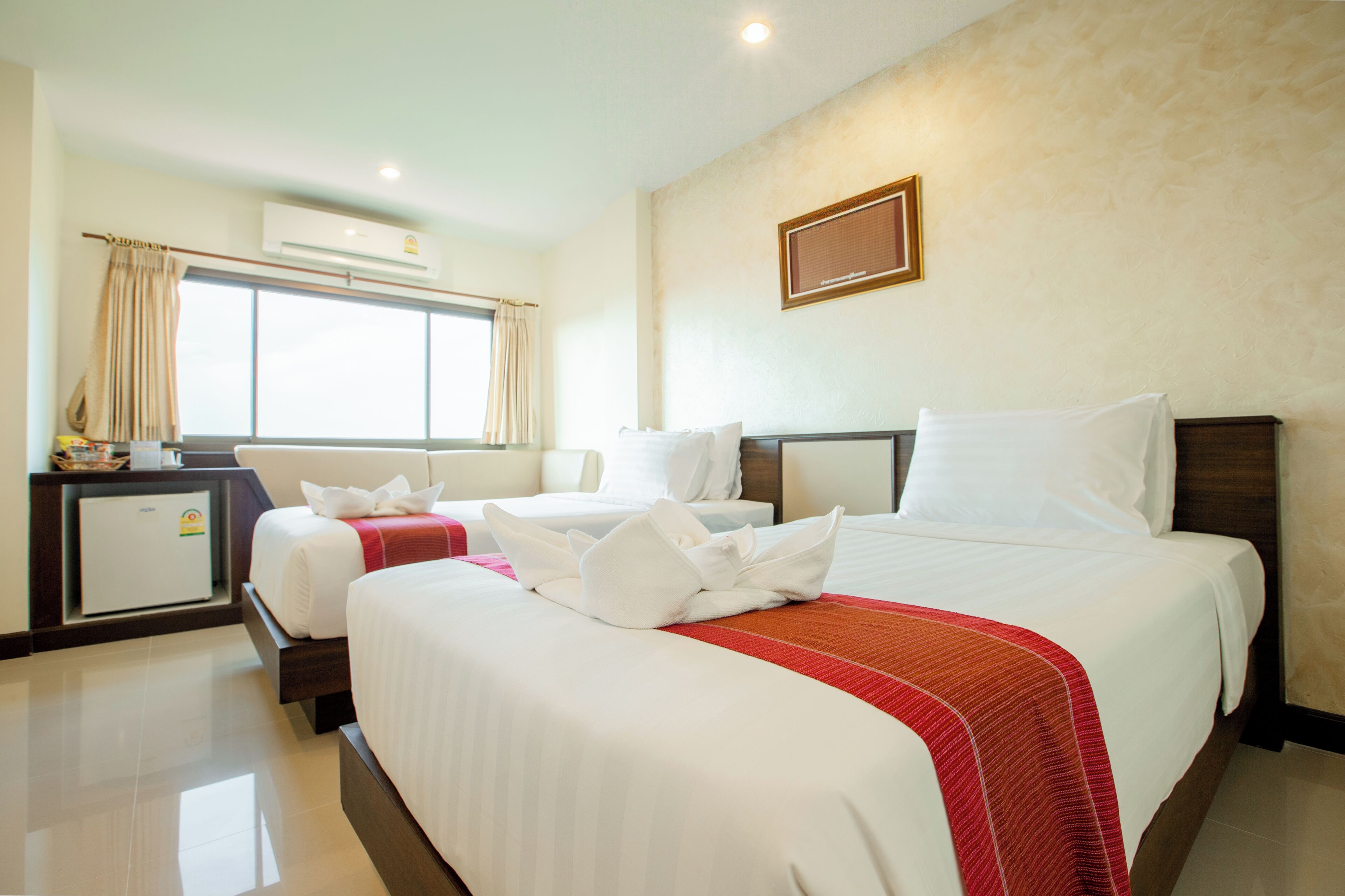 A hotel room with two beds, a desk, and an air conditioning unit.