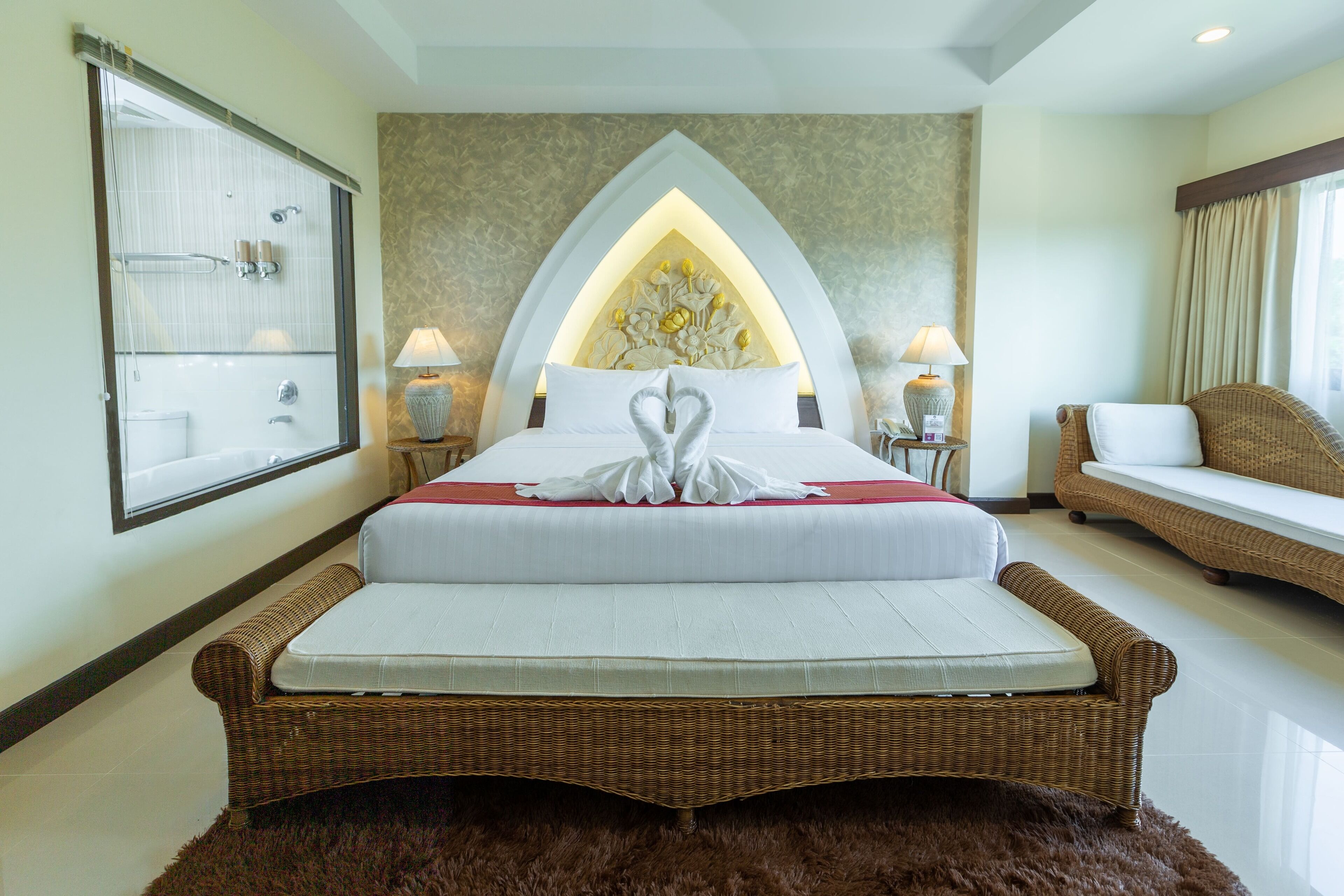 A hotel room with a large bed, a wicker sofa, a small table with a lamp, and a mirror on the wall.