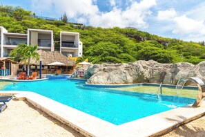 A swimming pool with a rock feature, lounge chairs, and a building with balconies.