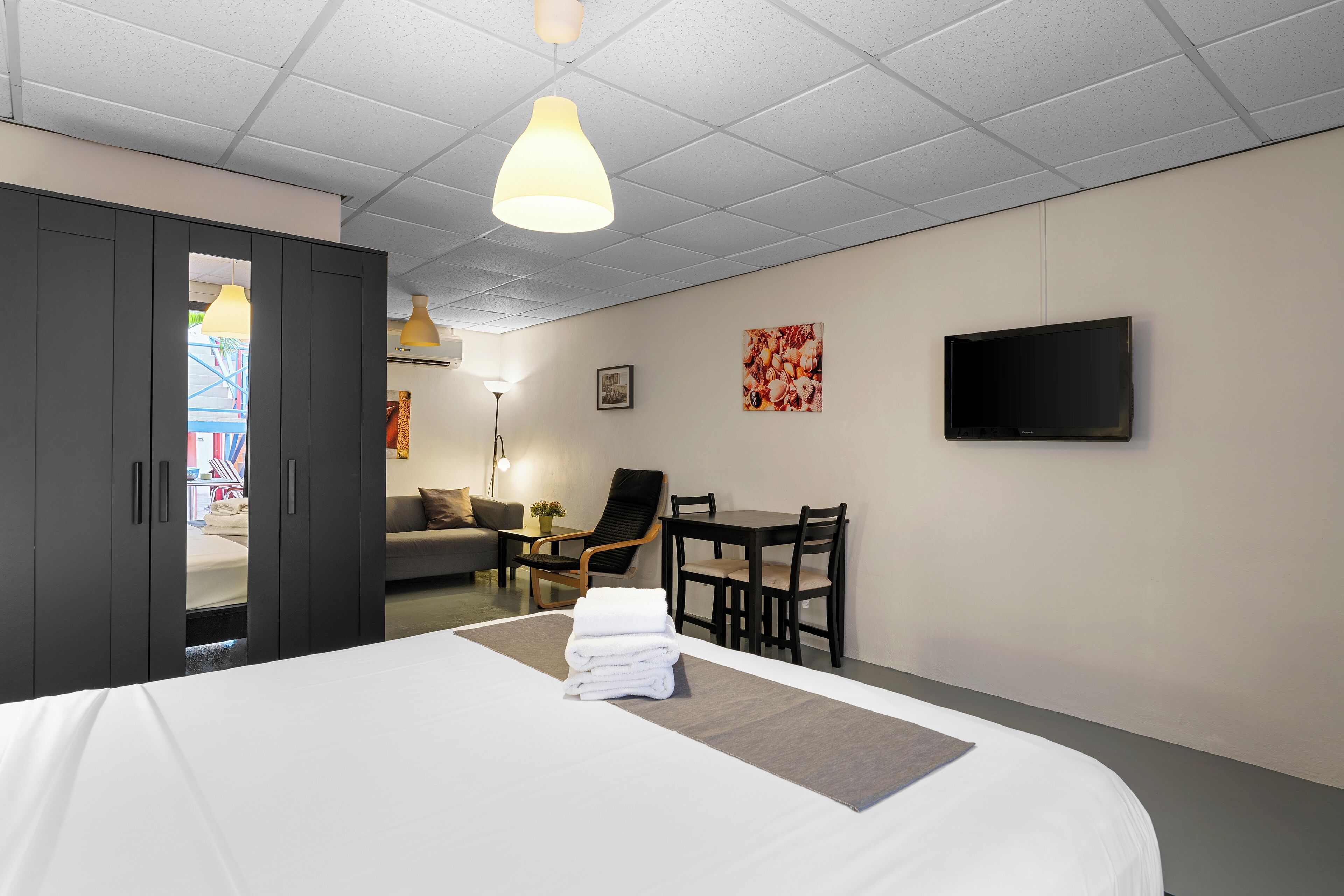 A hotel room with a bed, a desk, a chair, a TV, and a wardrobe.