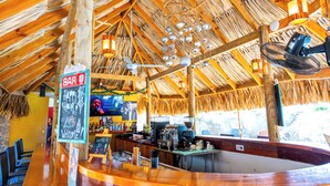 A bar area with a wooden ceiling, bar stools, and a counter with a cash register. - The Ritz Village Hotel  (Willemstad)