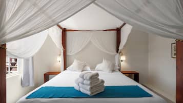 Un lit à baldaquin à quatre poteaux, agrémenté de draps blancs et d’une pile de serviettes posées sur un chemin de lit bleu.