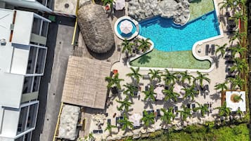 Vista aérea de un resort con piscina, palmeras y sillones de descanso.