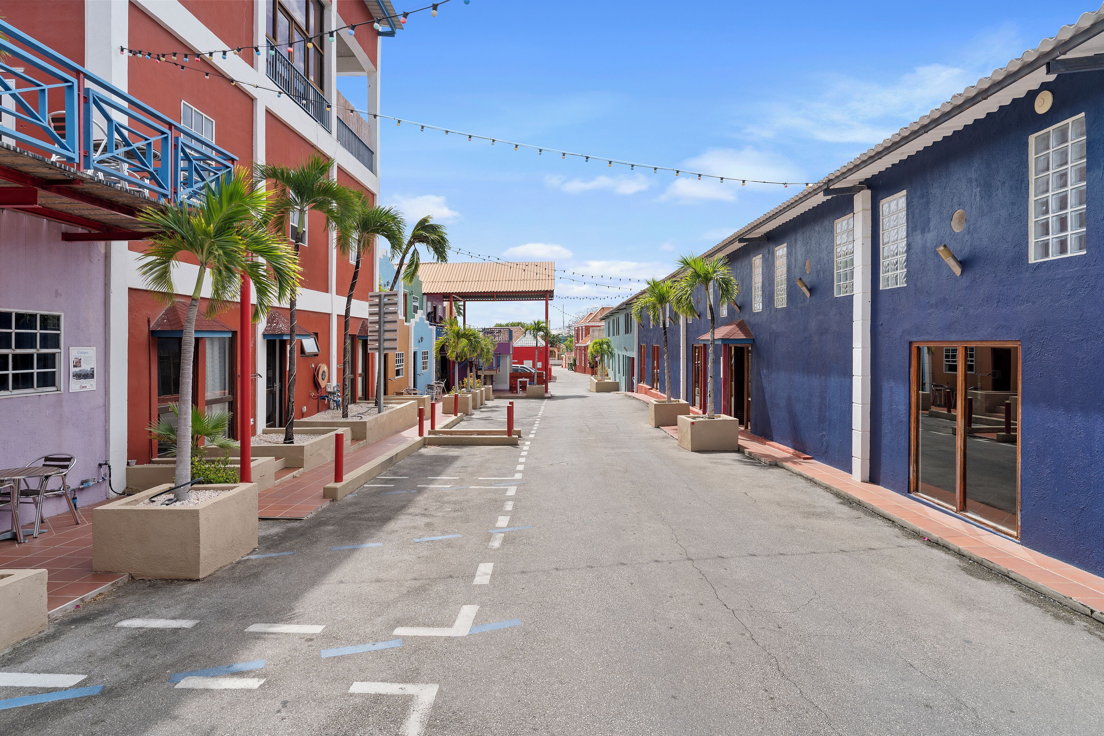 A street lined with colorful buildings, palm trees, and a clear sky.