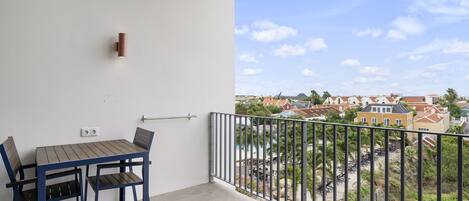 Un balcón con mesa y sillas, barandilla y vista a una zona residencial.