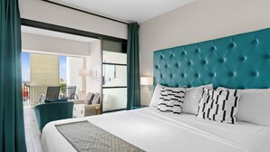 A hotel room with a large bed, a teal headboard, and a view through a glass door to the outside. - The Ritz Village Hotel  (Willemstad)