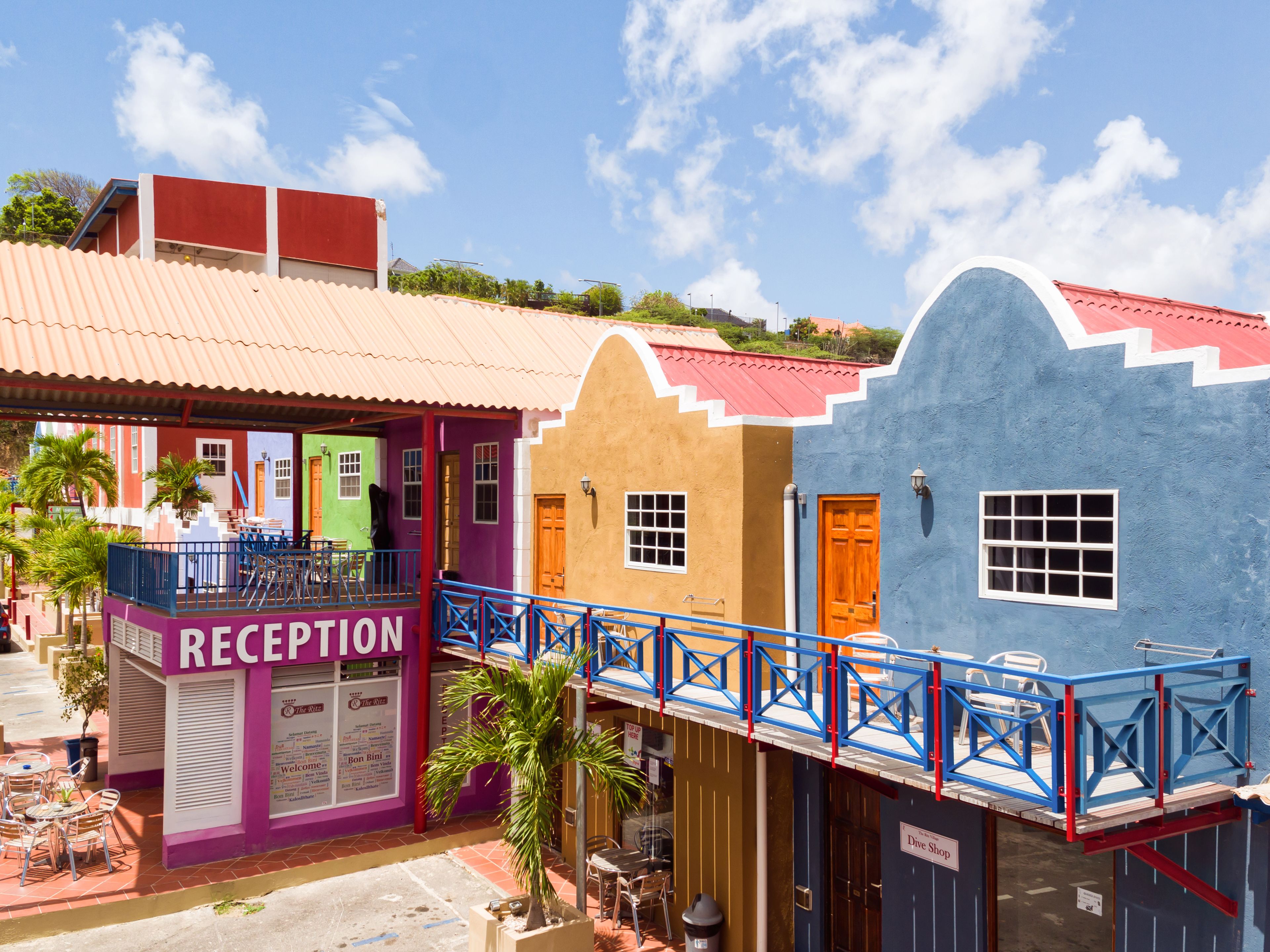 A colorful building with a reception area, a balcony, and a blue building with a 'Dive Shop' sign.