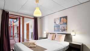 A hotel room with a large bed, a bedside table, a nightstand, a ceiling light, and a wall art piece. - The Ritz Village Hotel  (Willemstad)
