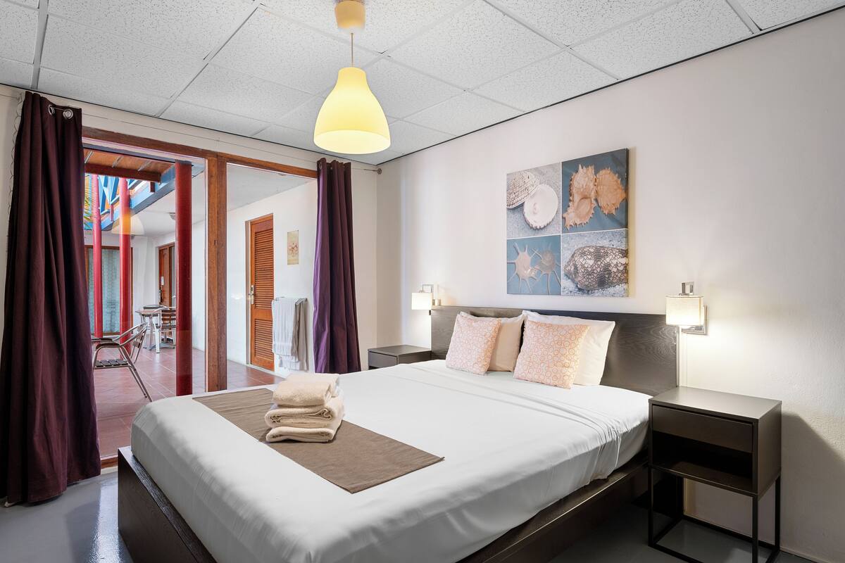 Habitación de hotel con una cama grande, una mesita de noche, una lámpara de techo y una obra de arte en la pared.