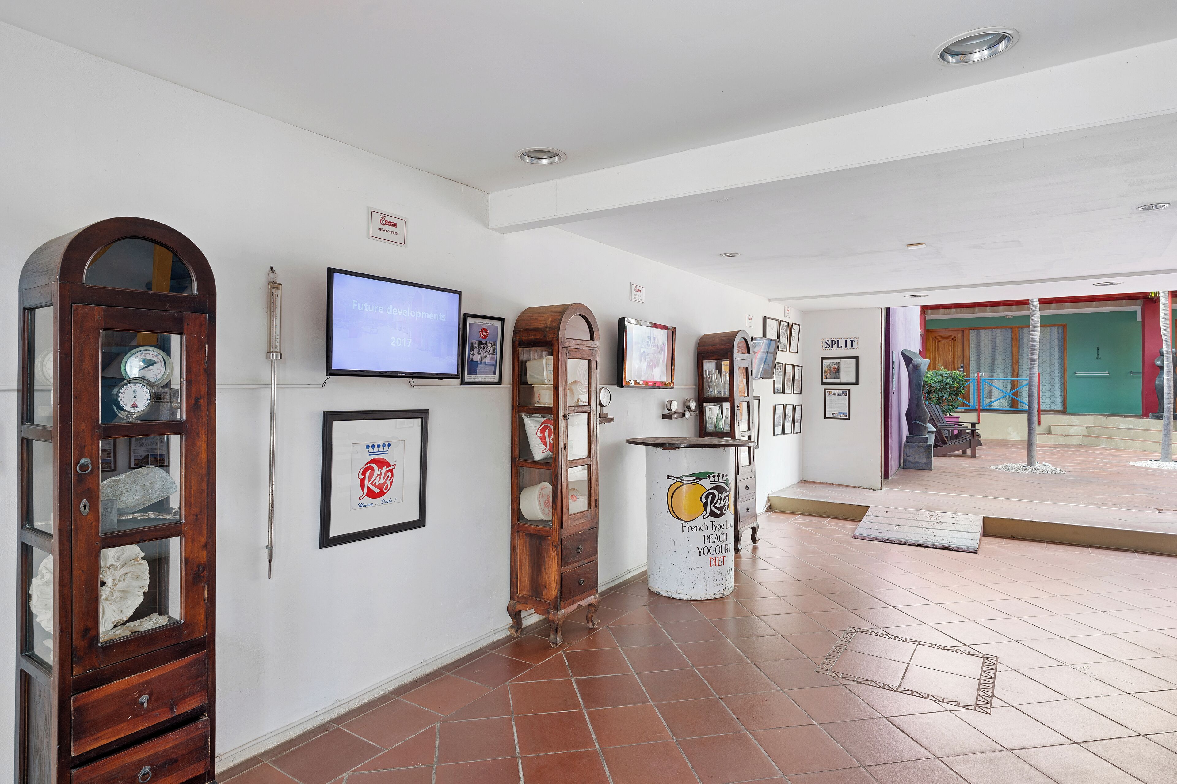 A hallway with a clock, a television, and framed pictures on the wall.
