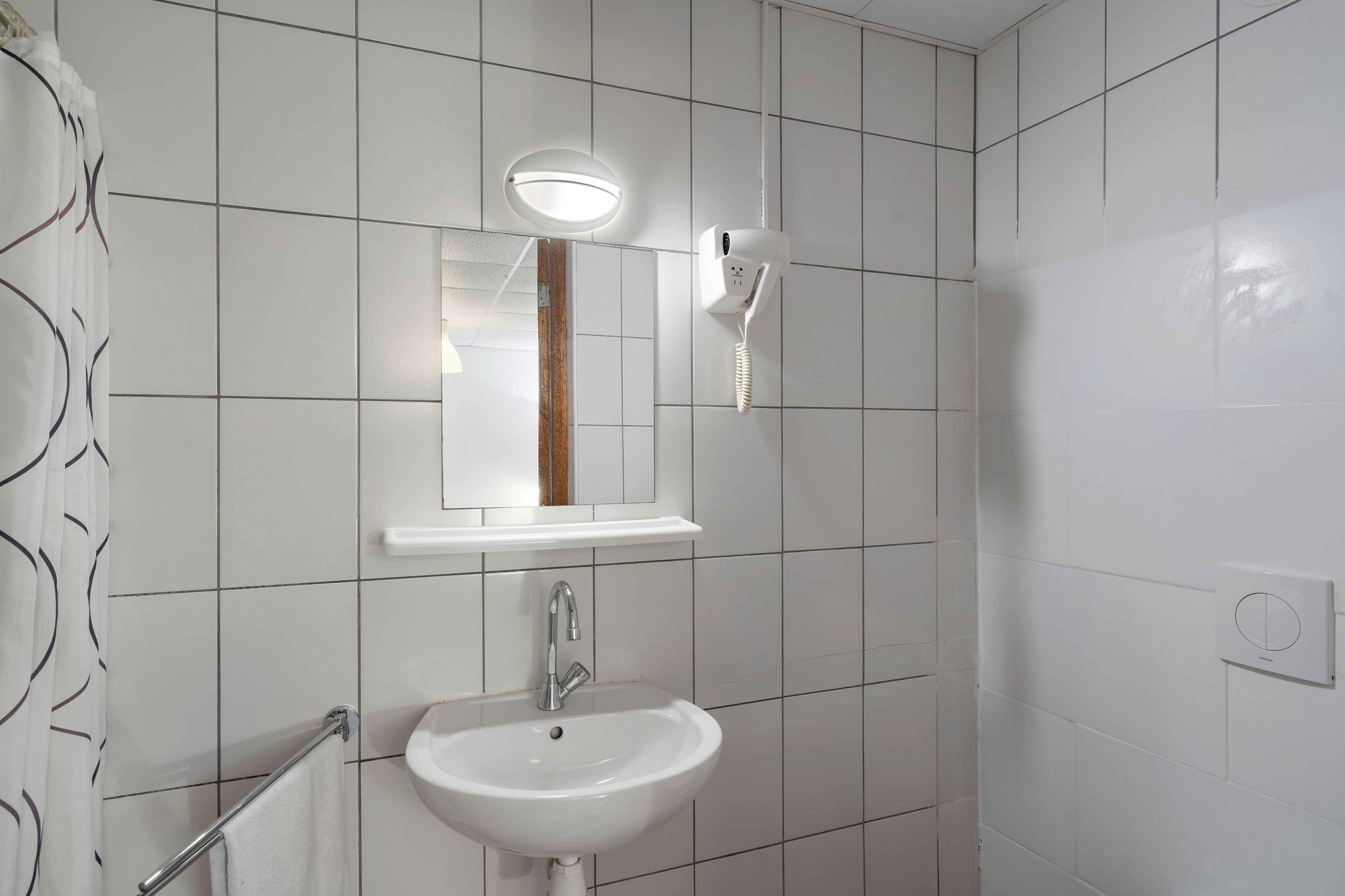 A bathroom with white tiled walls, a sink, a mirror, a towel rack, and a hairdryer mounted on the wall.