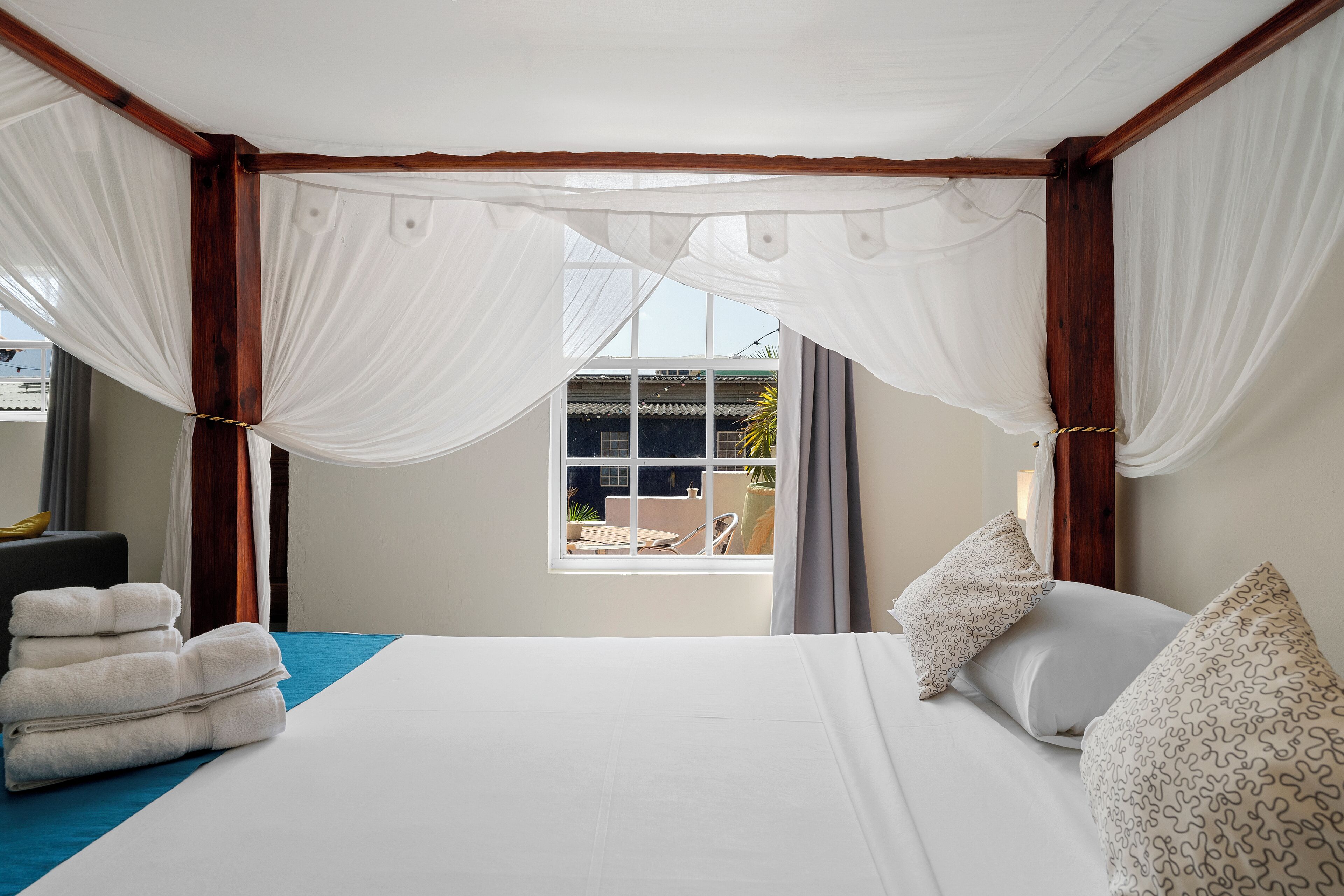 A hotel room with a bed, white curtains, and a view of the outside.