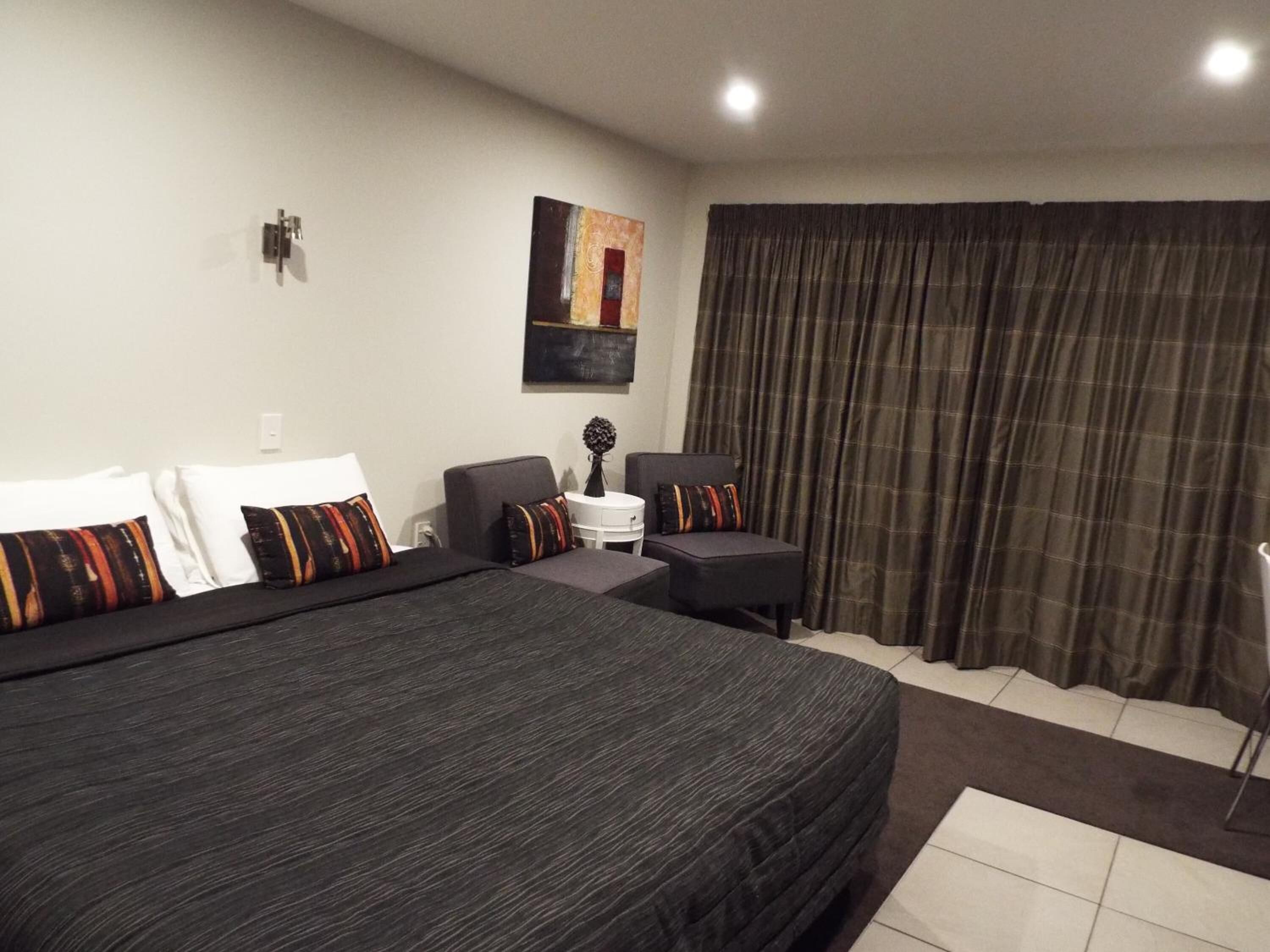 Una habitación de hotel con una cama grande, dos sillones, una mesita y un cuadro en la pared.