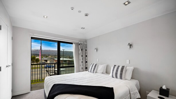 Ein modernes Hotelzimmer mit einem großen Bett, einem kleinen Nachttisch, einem Fenster mit Ausblick und einem Balkon.