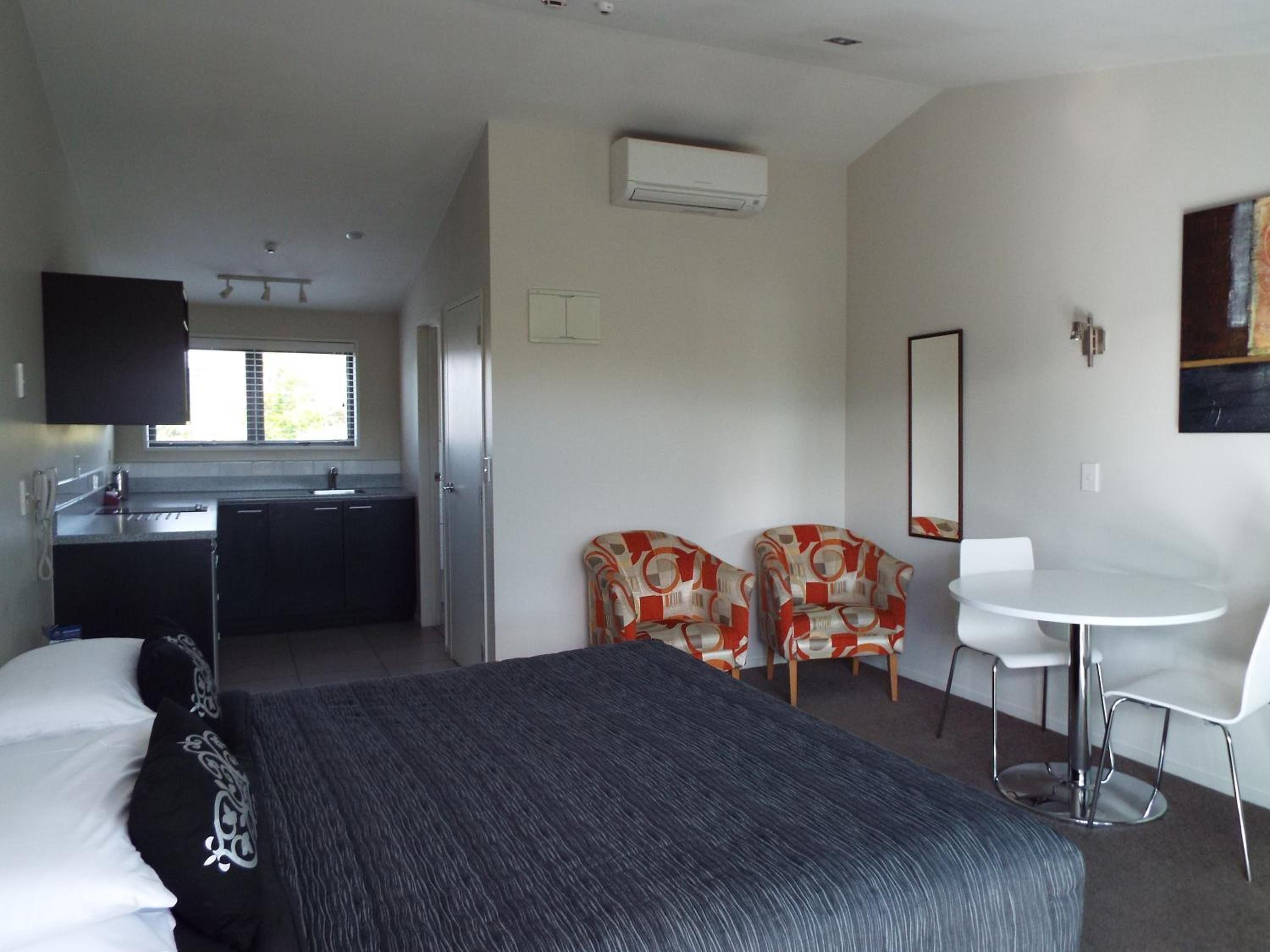 Habitación de hotel con cama, escritorio, dos sillas, kitchenette pequeña y ventana.