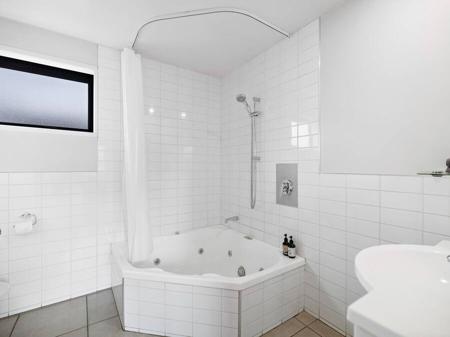 A modern bathroom with a white tiled wall, a large bathtub, a shower, and a toilet.
