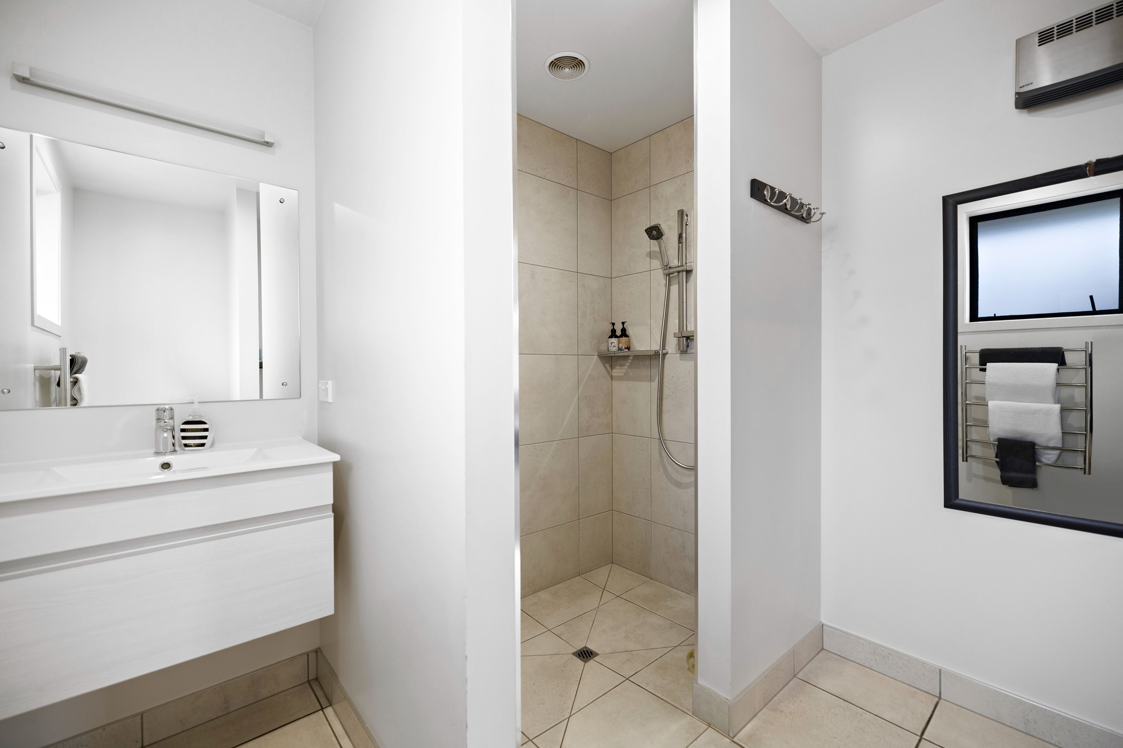 Un baño moderno con tocador blanco, ducha con cabezal de ducha de mano y barra para toallas.