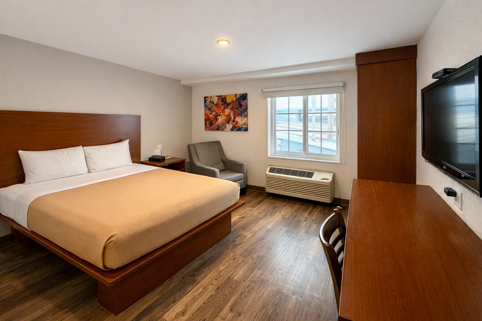 Habitación de hotel con una cama grande, un escritorio, una silla, un televisor, una ventana y un equipo de aire acondicionado.