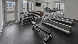 Un gimnasio con cintas de correr, mancuernas y un banco.