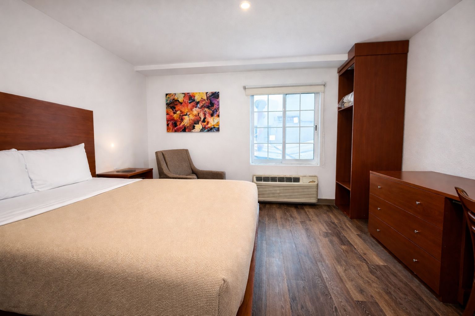 A bedroom with a large bed, a chair, a dresser, a window with blinds, and a colorful abstract painting on the wall.
