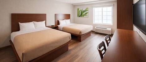 A hotel room with two beds, a desk, a TV, and a window with a plant.