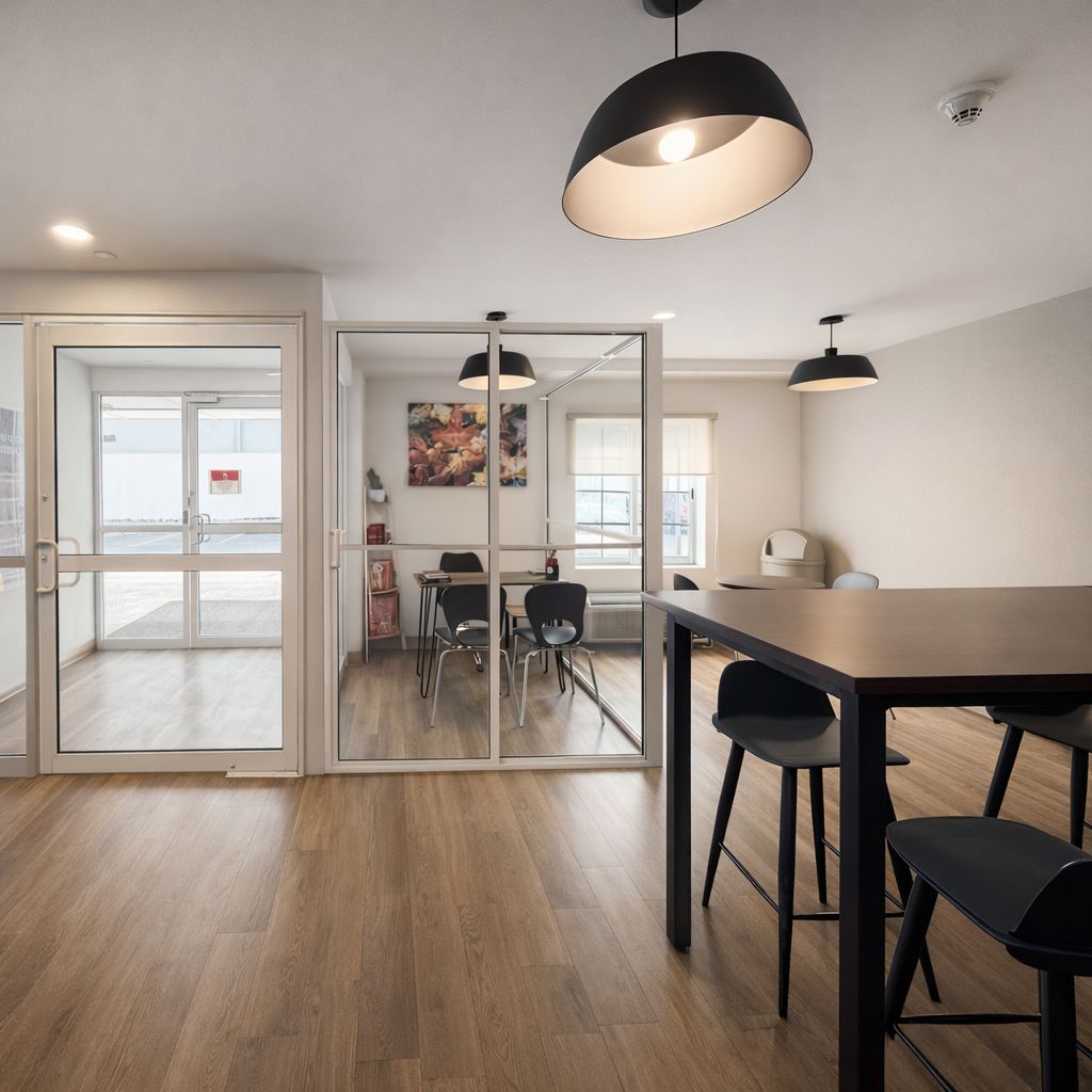 Un espacio interior con piso de madera, una mesa con sillas y una puerta de vidrio que da al exterior.