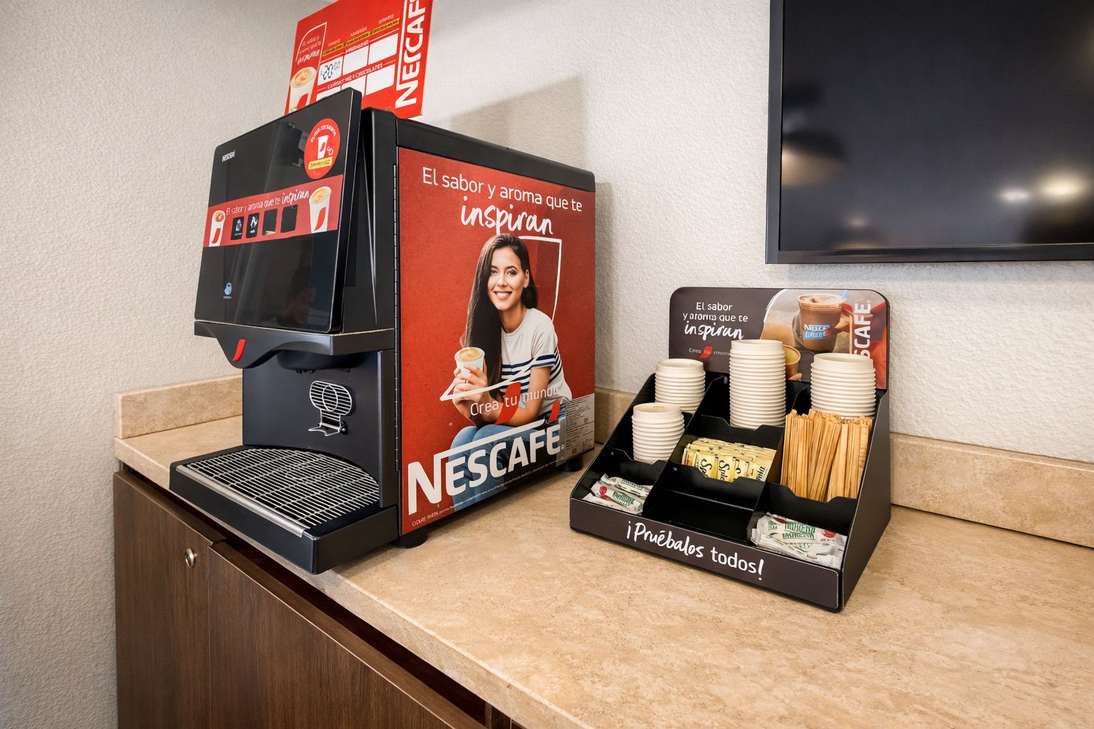 Una máquina de café Nescafé y una estación de café con vasos y cubiertos desechables.