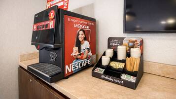 Una máquina de café Nescafé y una estación de café con vasos y cubiertos desechables.