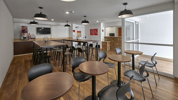 Un comedor moderno con varias mesas y sillas, una cafetera y una pared decorativa de piedra.