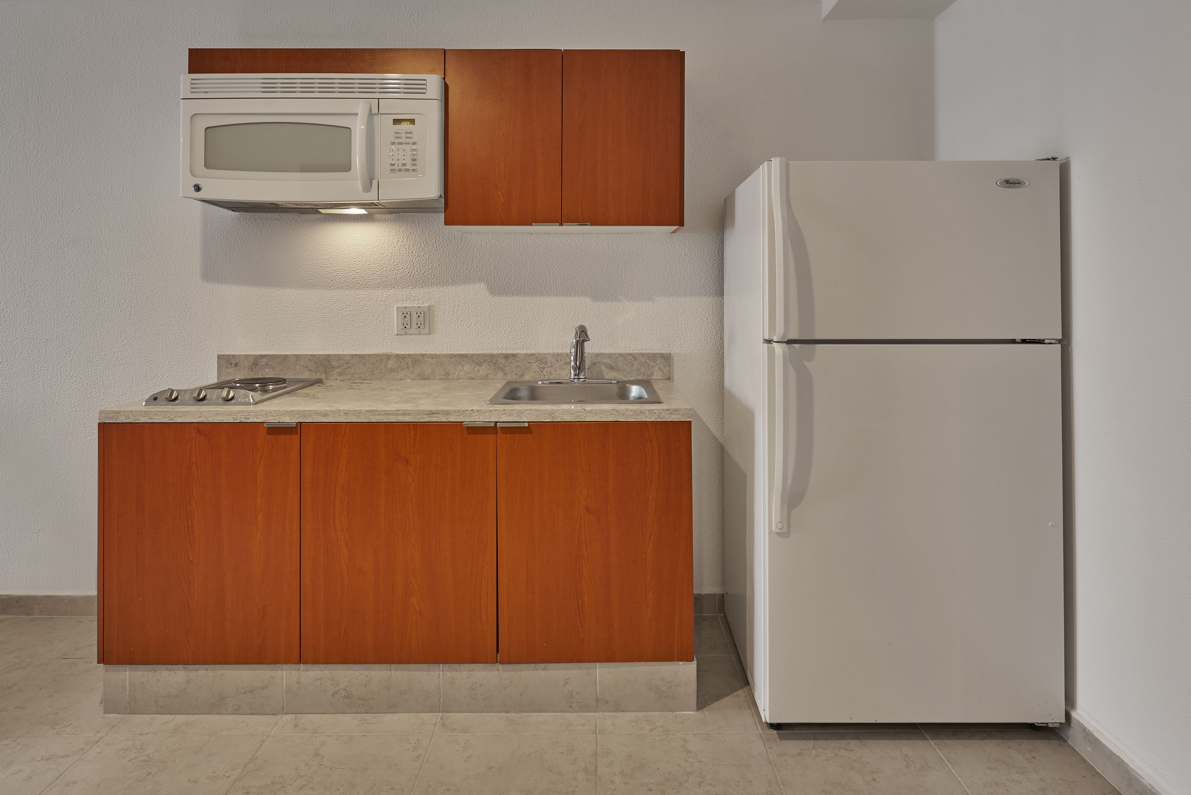A kitchen with wooden cabinets, a white microwave, a sink, and a white refrigerator.