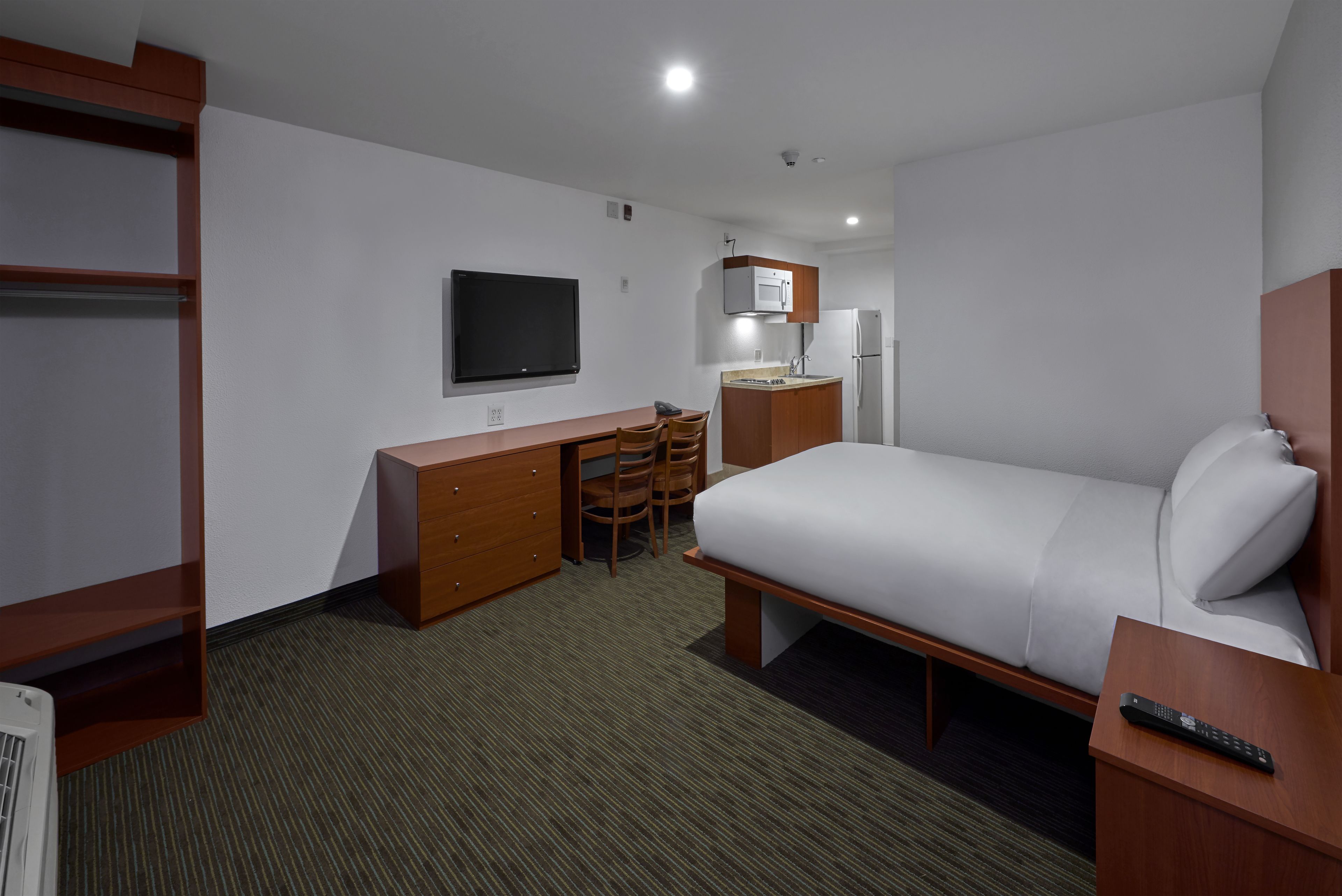 Une chambre d’hôtel équipée d’un lit, d’un bureau avec une chaise, d’une télévision, d’un four à micro-ondes et d’un réfrigérateur.