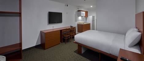 Habitación de hotel con cama, escritorio con silla, televisor, microondas y refrigerador.