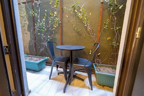 A small outdoor patio with a round table and two chairs, surrounded by a wire mesh fence and potted plants. - Balo (Istanbul)