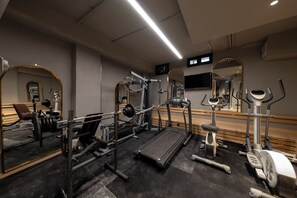 Ein Fitnessstudio mit Trainingsgeräten, Spiegeln und einem Fernseher.