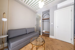 Un salon moderne avec un canapé gris, une table basse en verre et une armoire blanche.