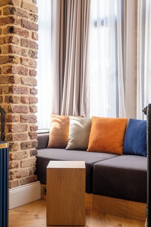 A room with a brick wall, a sofa with cushions, a wooden coffee table, and a window with curtains. - Balo (Istanbul)