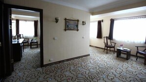 Hotelkamer met een kamerbreed tapijt, een zithoek met stoelen en een tafel, en een grote spiegel die de kamer weerspiegelt.