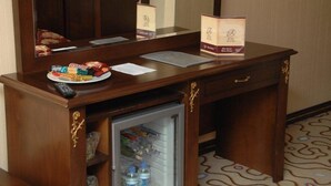 Een hotel bureau met een afstandsbediening, een schaal lekkernijen, een notitieboekje en een kleine koelkast.