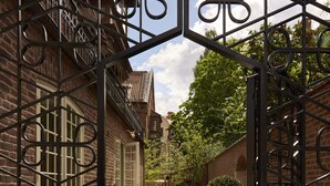 Un bâtiment en briques doté d’une entrée fermée par un portail, d’un chemin pavé et de haies bien entretenues.