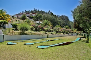 Espaço com mesas de bilhar e um jardim paisagístico com diversas plantas e árvores.