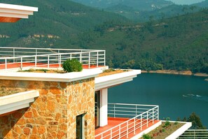 A modern building with stone walls and a balcony overlooking a lake.