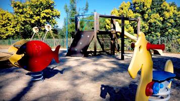 Explore the outdoor play area with a slide and climbing elements surrounded by lush trees.