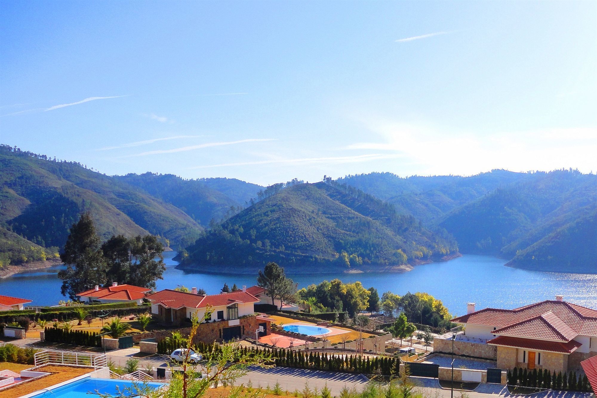 A coastal residential area with houses, a swimming pool, and a lake surrounded by hills.