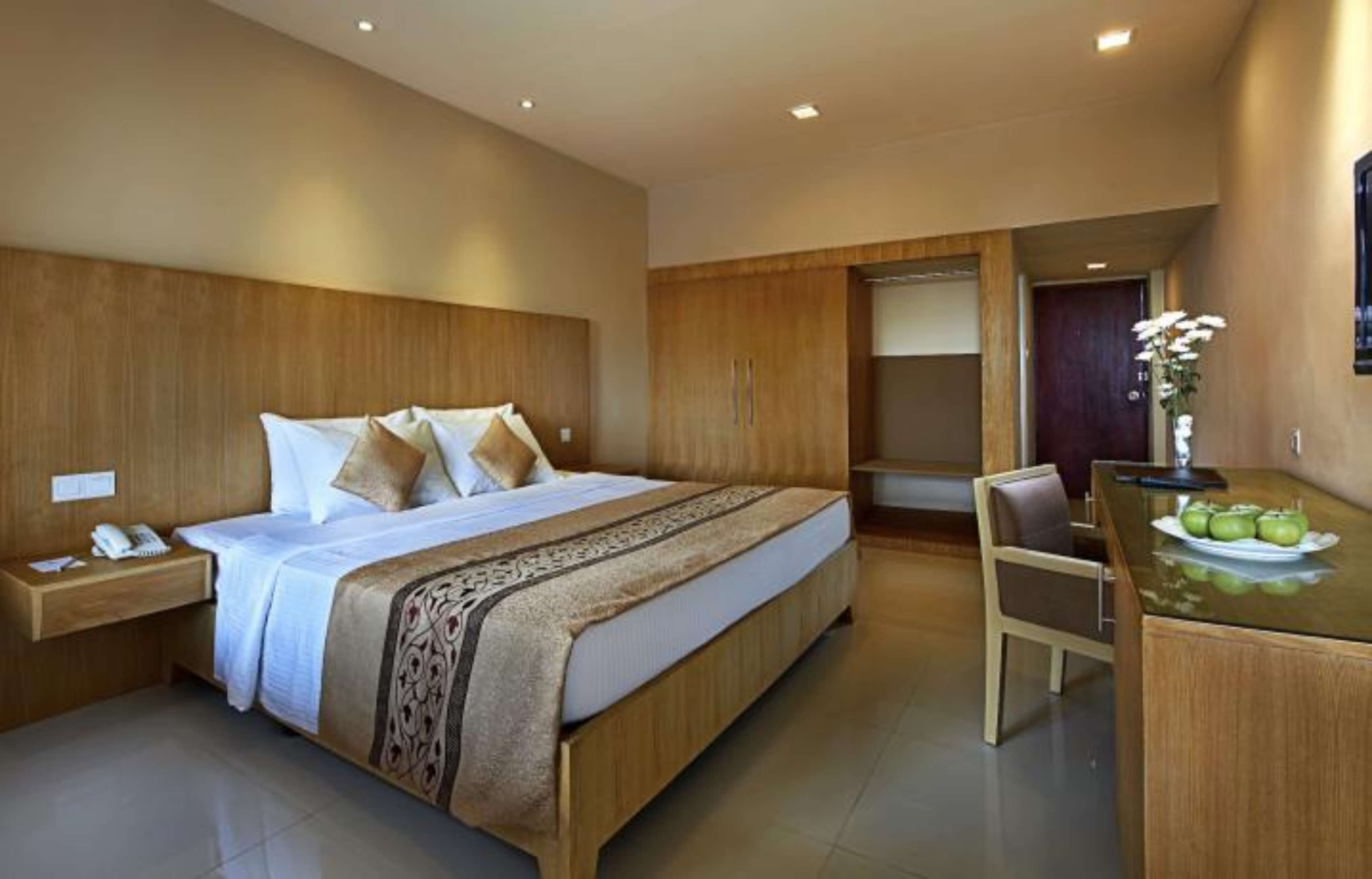 Una habitación de hotel moderna con una cama grande, cabecera de madera, un escritorio con una silla y una pequeña mesa con manzanas.