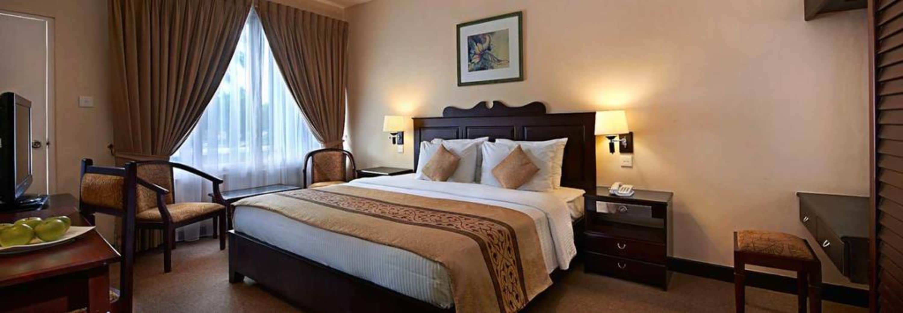 A hotel room with a large bed, two bedside tables, a chair, a desk, and a window with curtains.