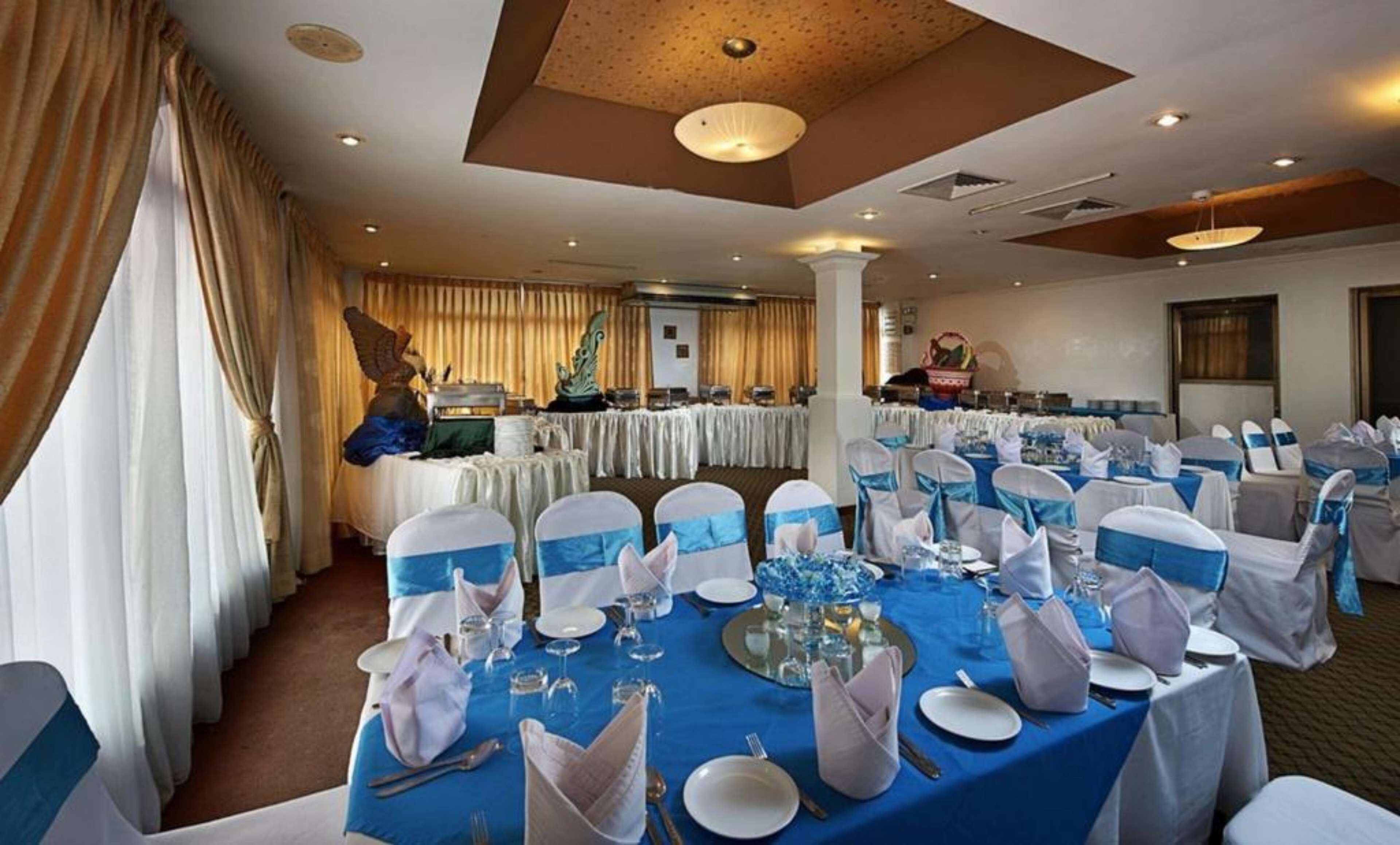 A banquet hall with round tables set for a formal event, featuring blue and white tablecloths and chairs with blue sashes.