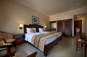 Habitación de hotel con una cama grande, dos mesitas de noche, un escritorio y una silla. Se puede ver un armario y un espejo en la pared.