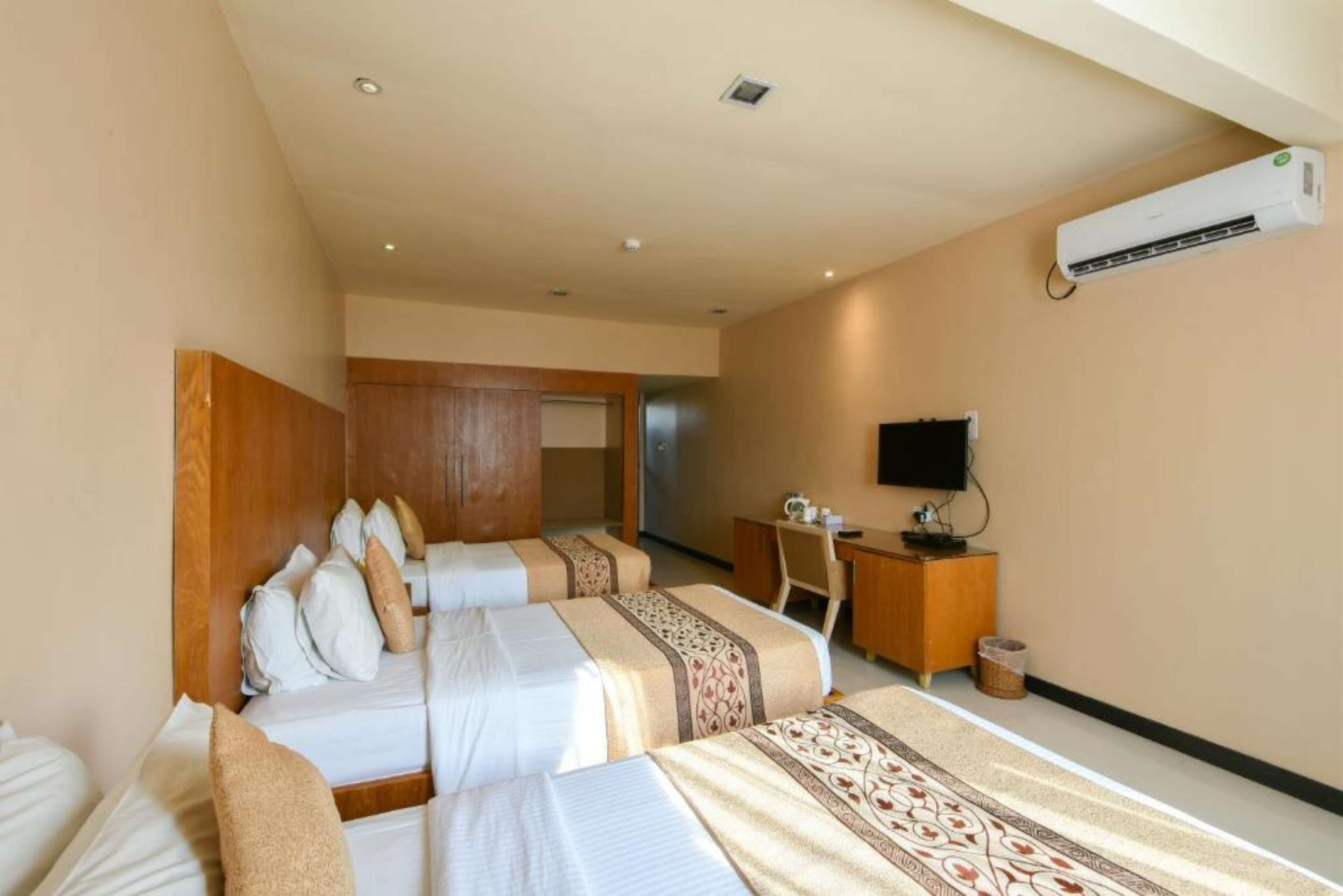 A hotel room with two beds, a desk, a chair, an air conditioner, and a television.