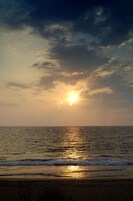 Una puesta de sol sobre una playa con olas y un cielo nublado.