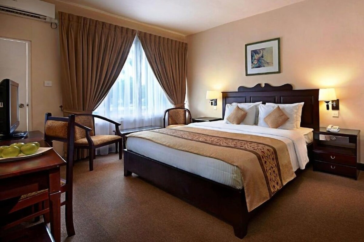 A hotel room with a bed, a desk with a chair, a television, and a window with curtains.
